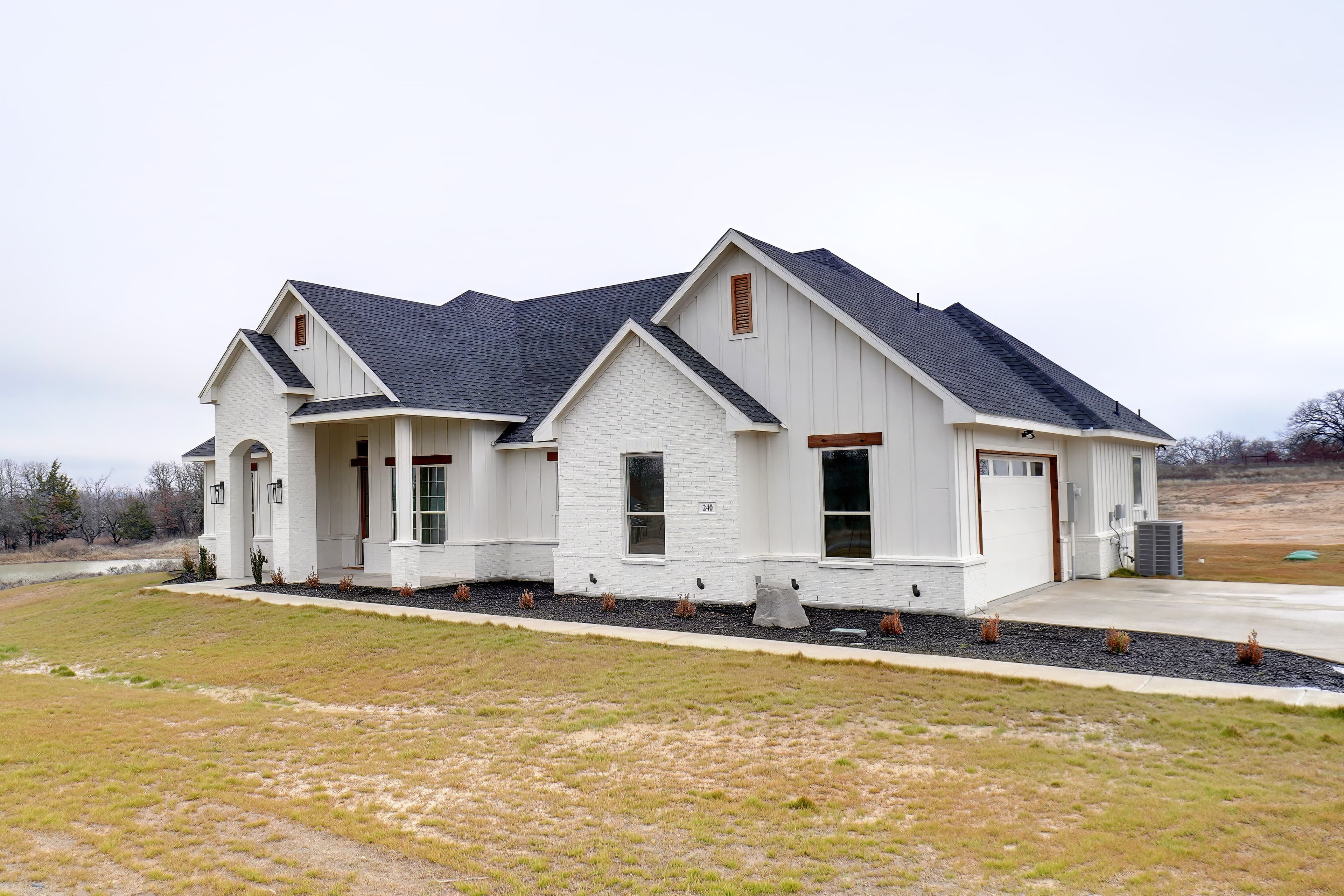 Modern white farmhouse with multiple gables and a dark grey roof on a grassy lot.