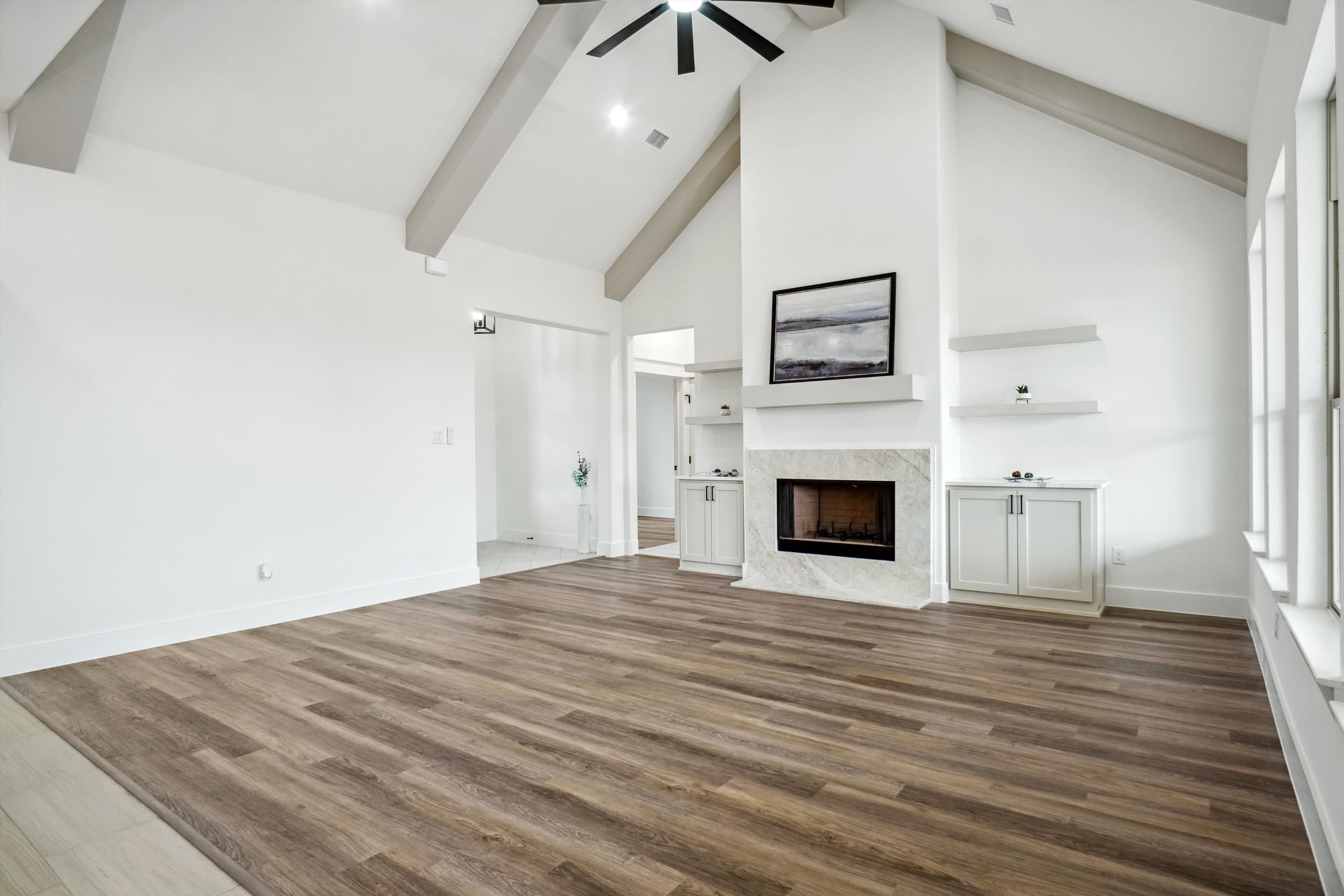 Modern living room with vaulted ceilings, wood floors, and a marble fireplace with built-in cabinets.
