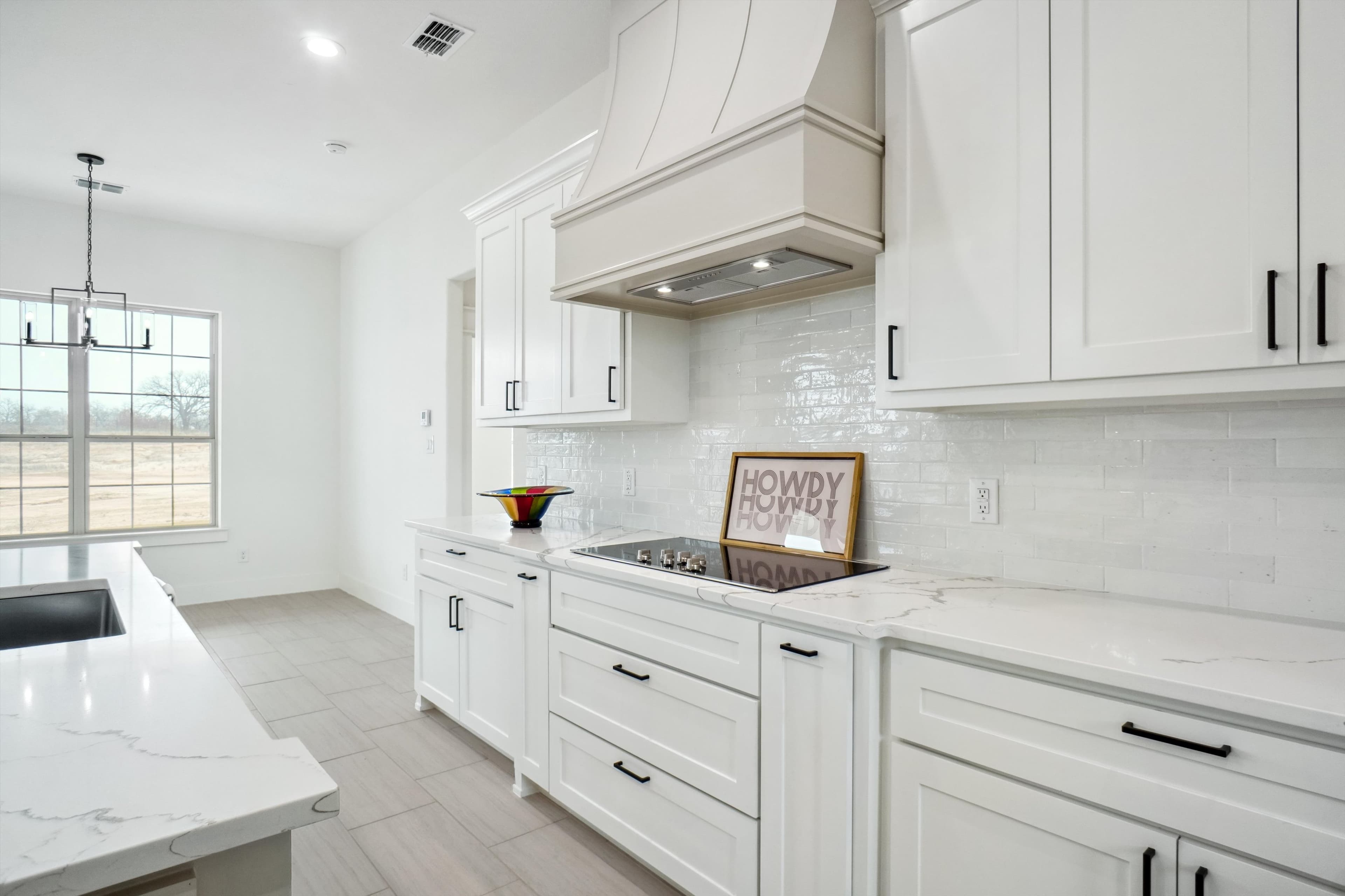 Bright white kitchen featuring marble countertops, subway tile backsplash, white cabinetry, and a black stovetop.