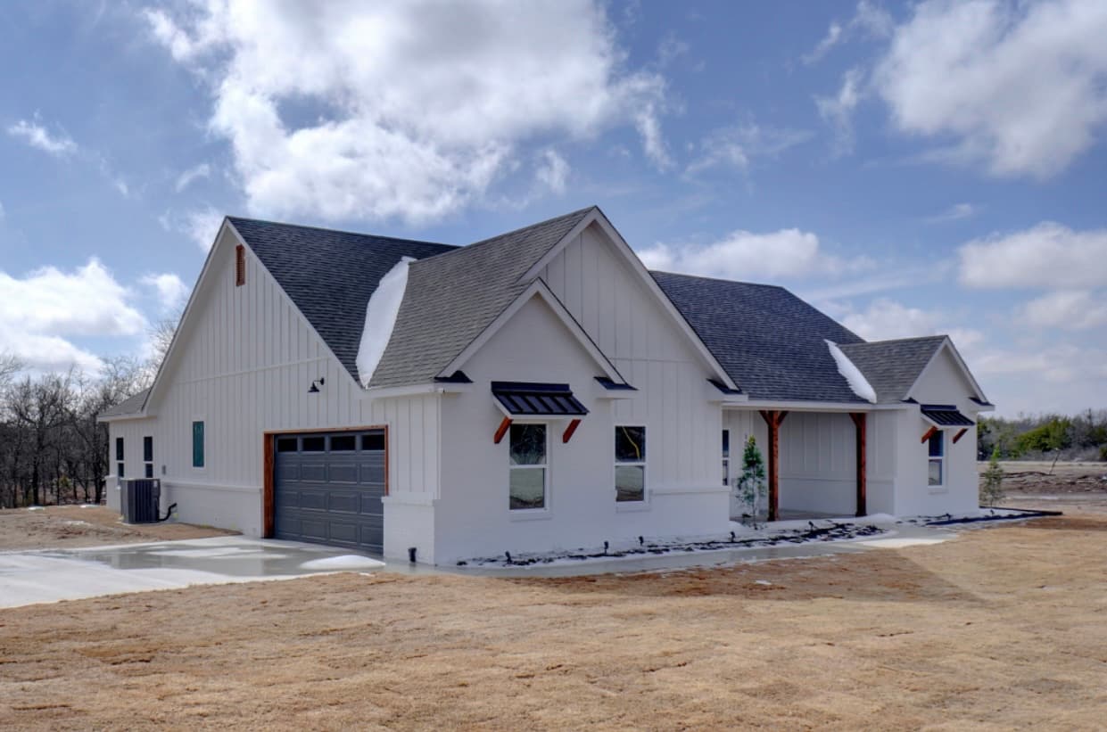 Modern white farmhouse with dark grey roof and garage door on a dry winter lawn.