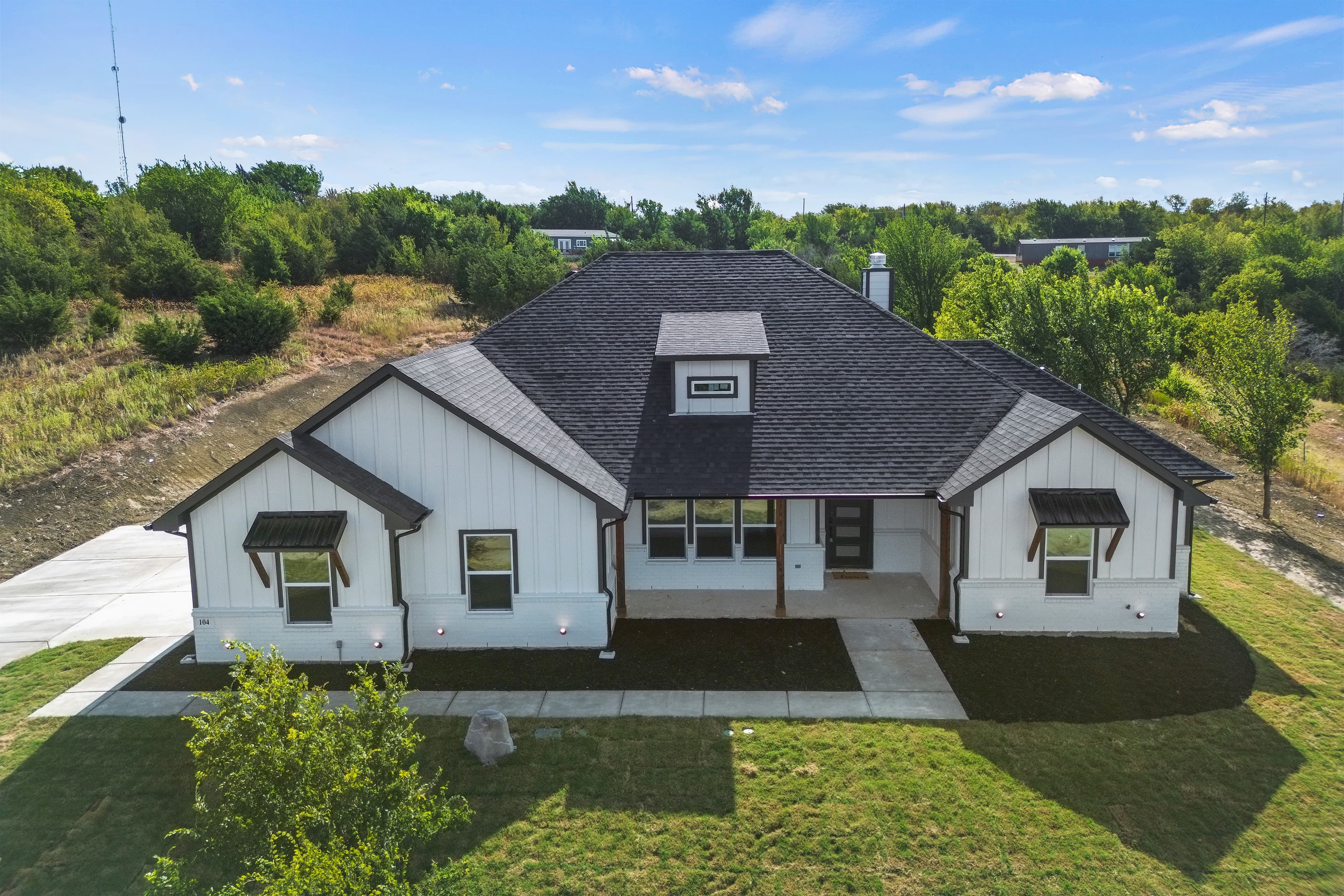 Modern white farmhouse with a dark roof, gabled peaks, black awnings, and green lawn.