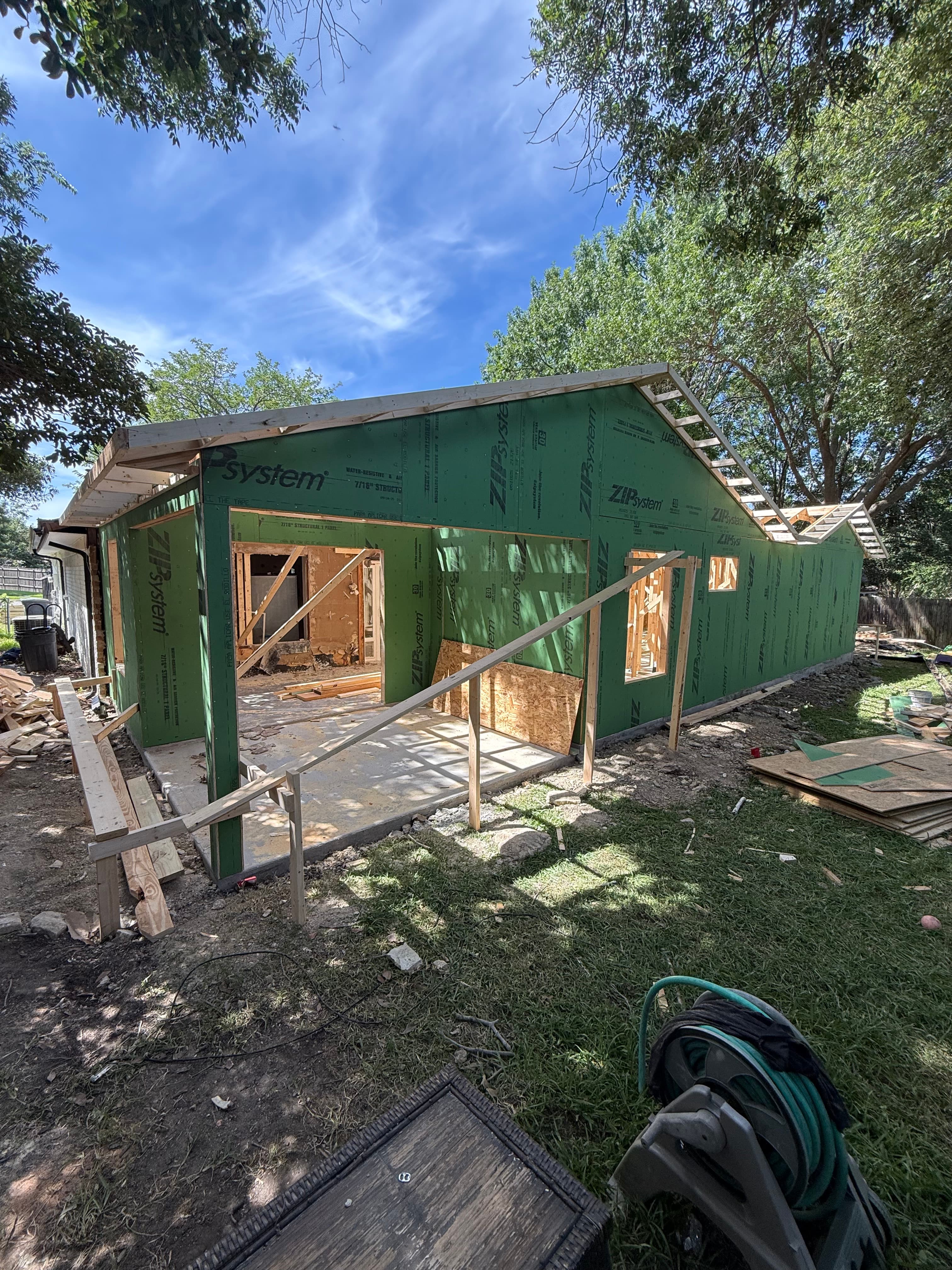 House under construction with green ZIP System sheathing and wooden framing against a blue sky.