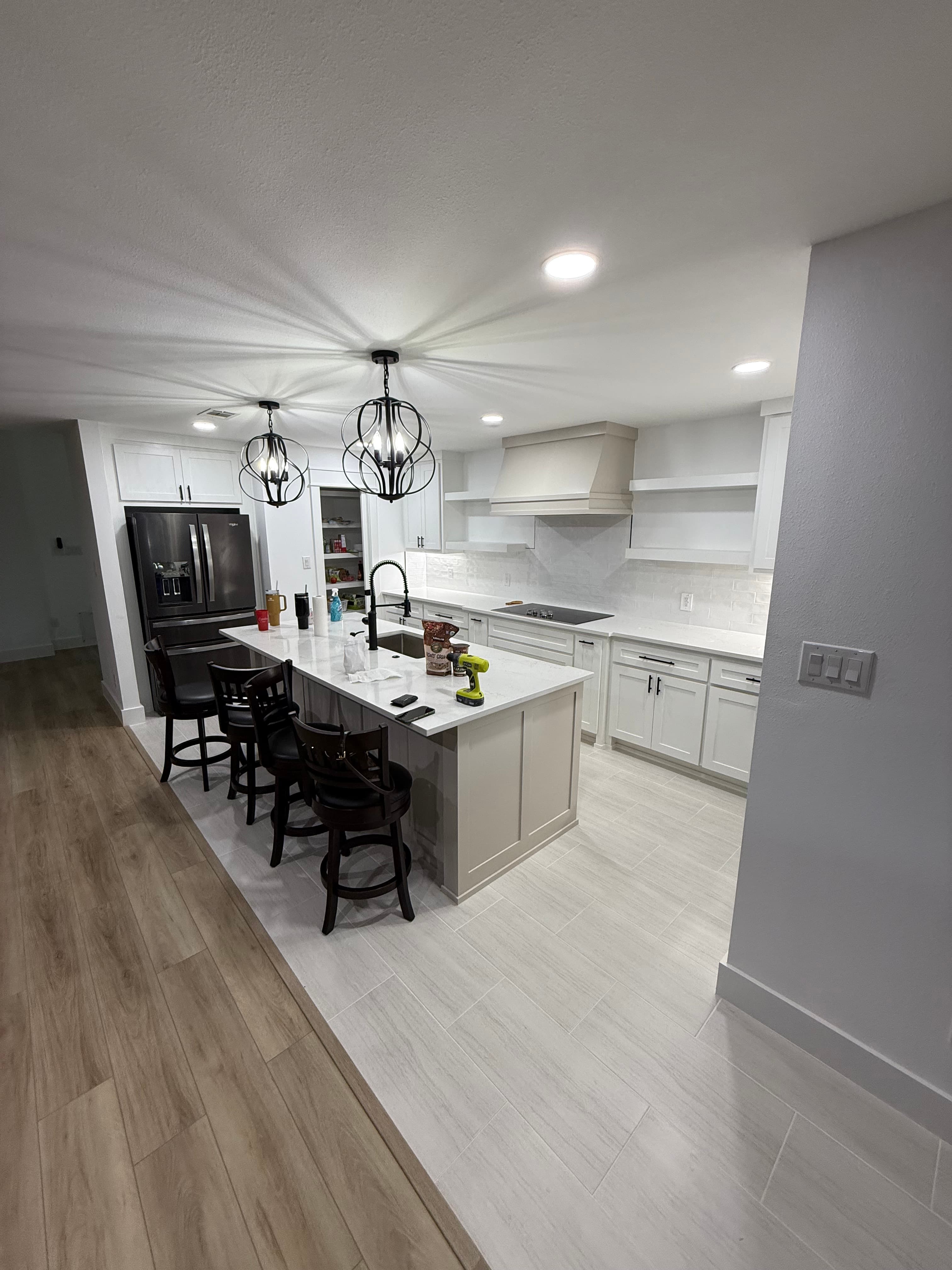 Modern white kitchen featuring a central island, black bar stools, and orb pendant lights.