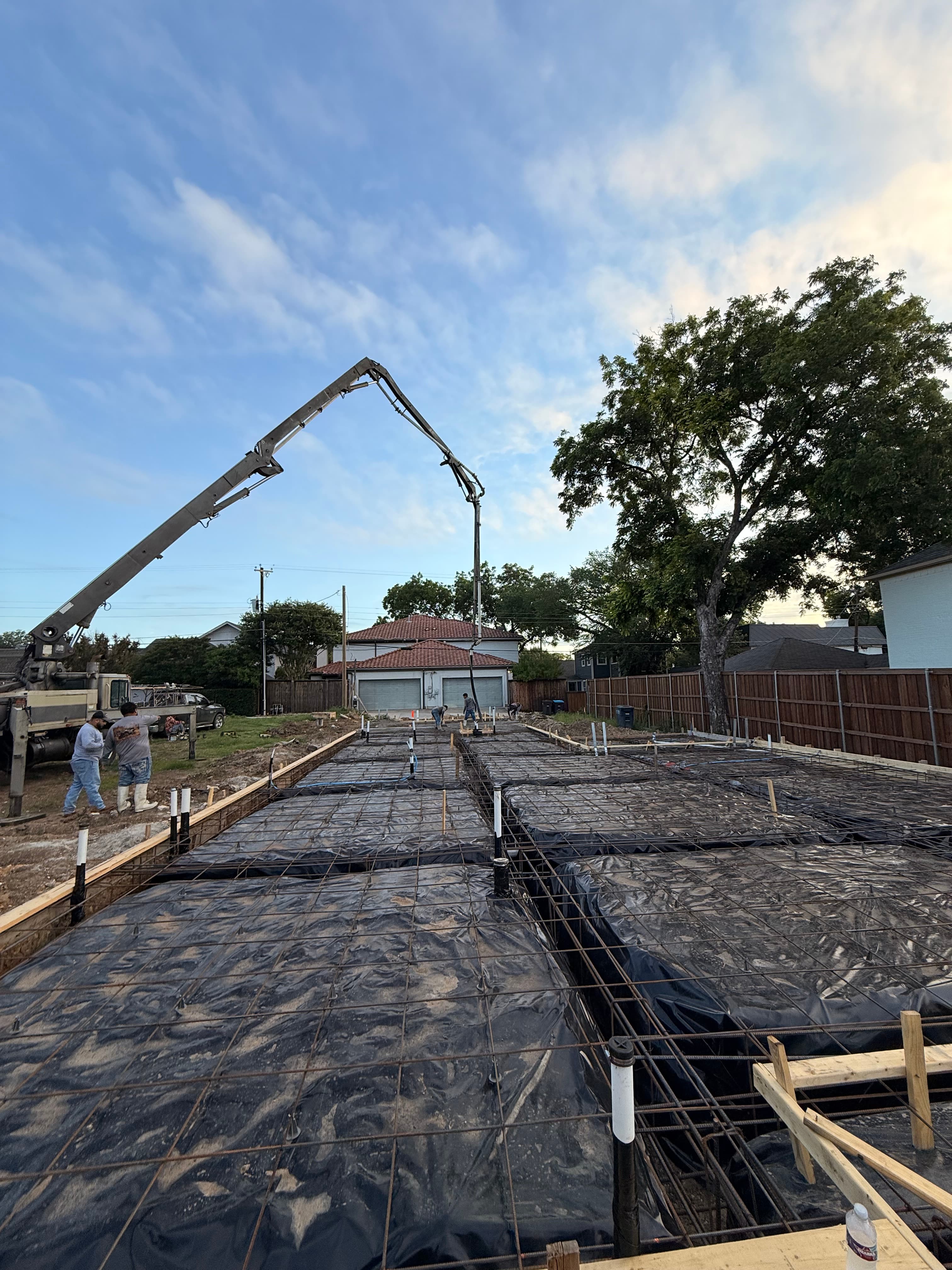 Concrete pump truck boom extends over a residential foundation with rebar and black plastic sheeting.