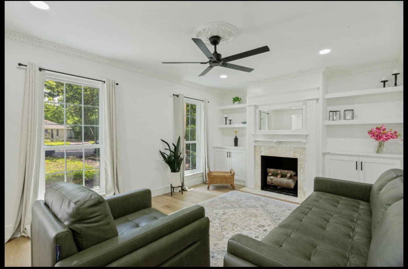 Bright living room featuring olive green leather sofas, a white fireplace, and large windows.