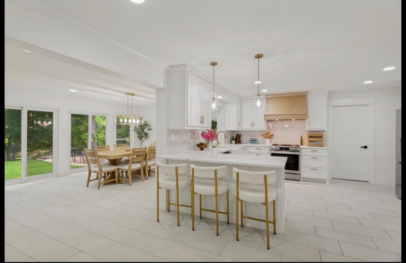 Modern white kitchen with gold hardware, bar stools, and open dining area with sliding doors.