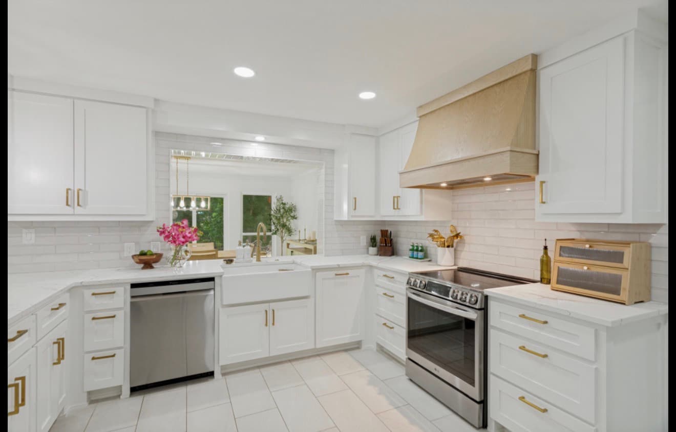 Modern white kitchen with gold hardware, stainless steel appliances, and a natural wood range hood.