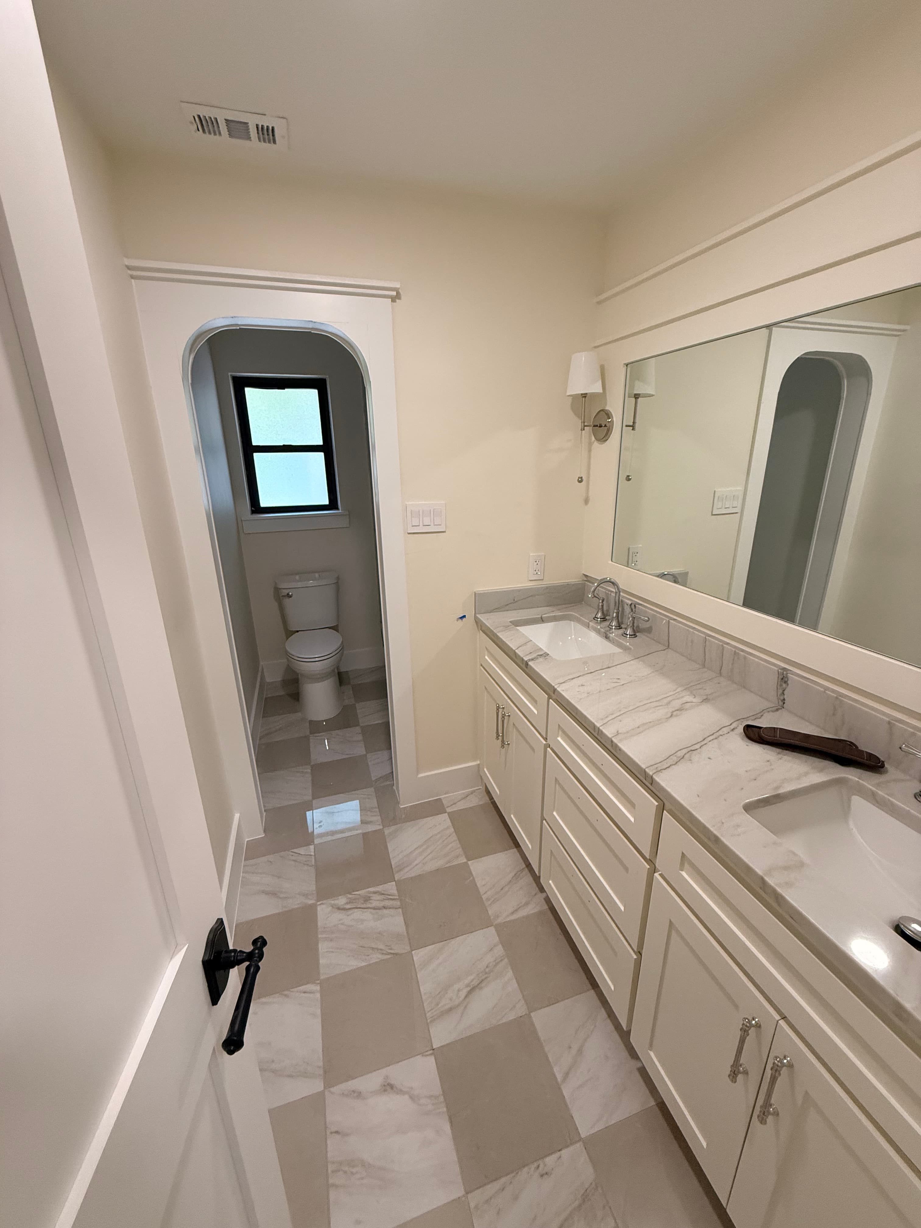 Modern bathroom with double marble vanity, checkered tile floor, and arched doorway to the toilet.